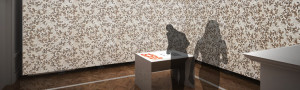 Computer rendering of a man drawing on a table. Around him on the walls are an all-over beige pattern.