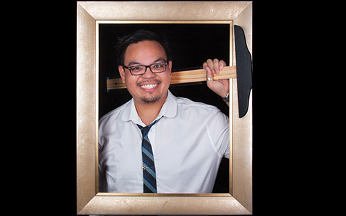 young man in glasses and a white collared shirt, smiling and holding a T-square