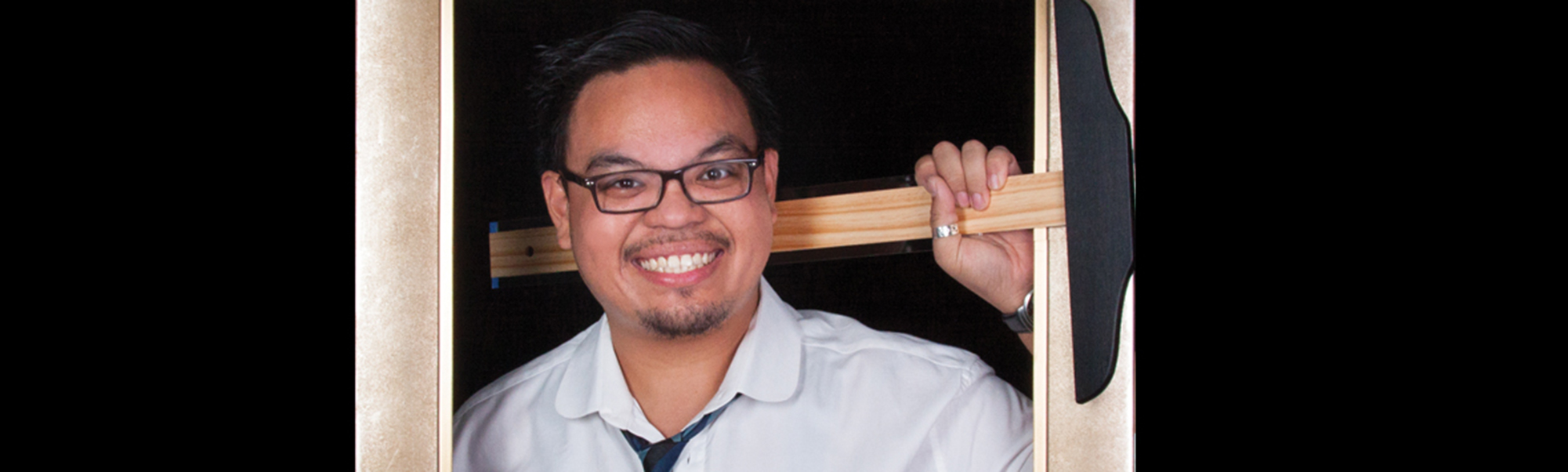 young man in glasses and a white collared shirt, smiling and holding a T-square