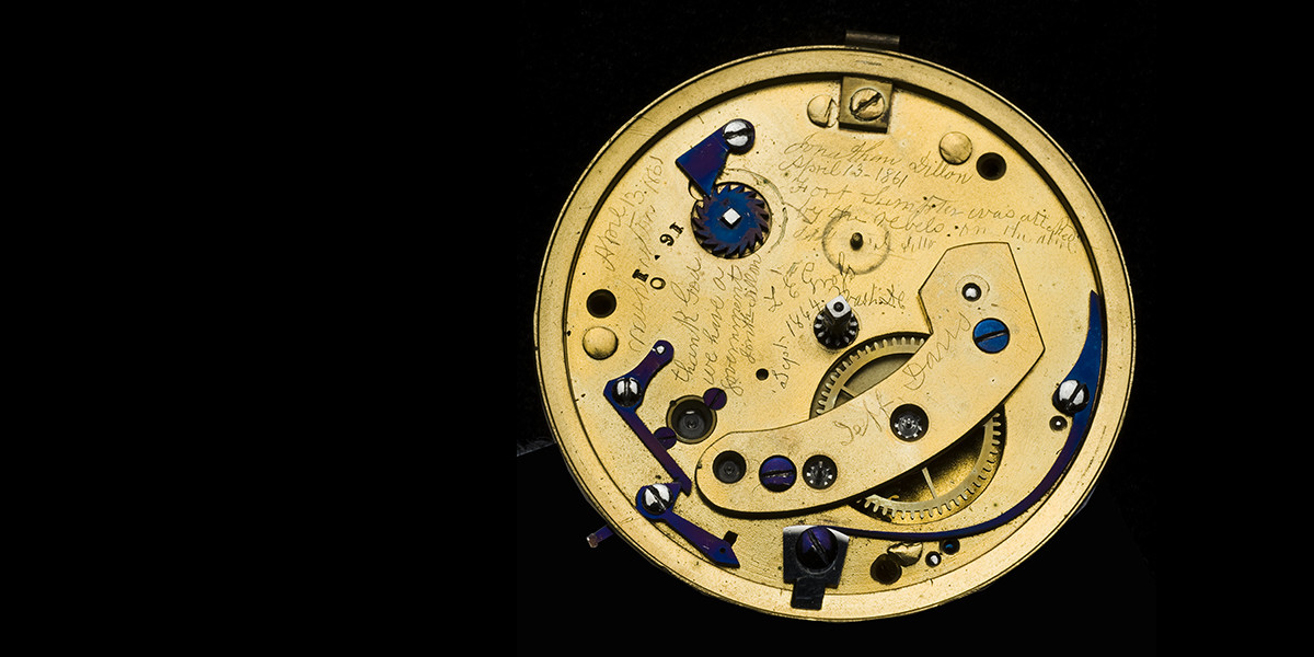 inside of an old watch, gold in color, with lots of casually engraved inscriptions inside, as if no one were intended to see them
