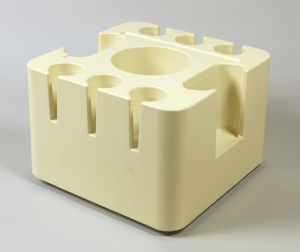 Molded cube shape of off-white plastic, casters; large cylindrical well in center, three smaller wells on two sides, one oval well on each of other two sides.