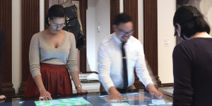 Four young adults gathered around a large touchscreen table, immersed in their activities, in a gallery setting.