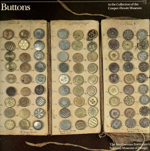 a grid of many old-looking buttons of different materials laid out on cloth