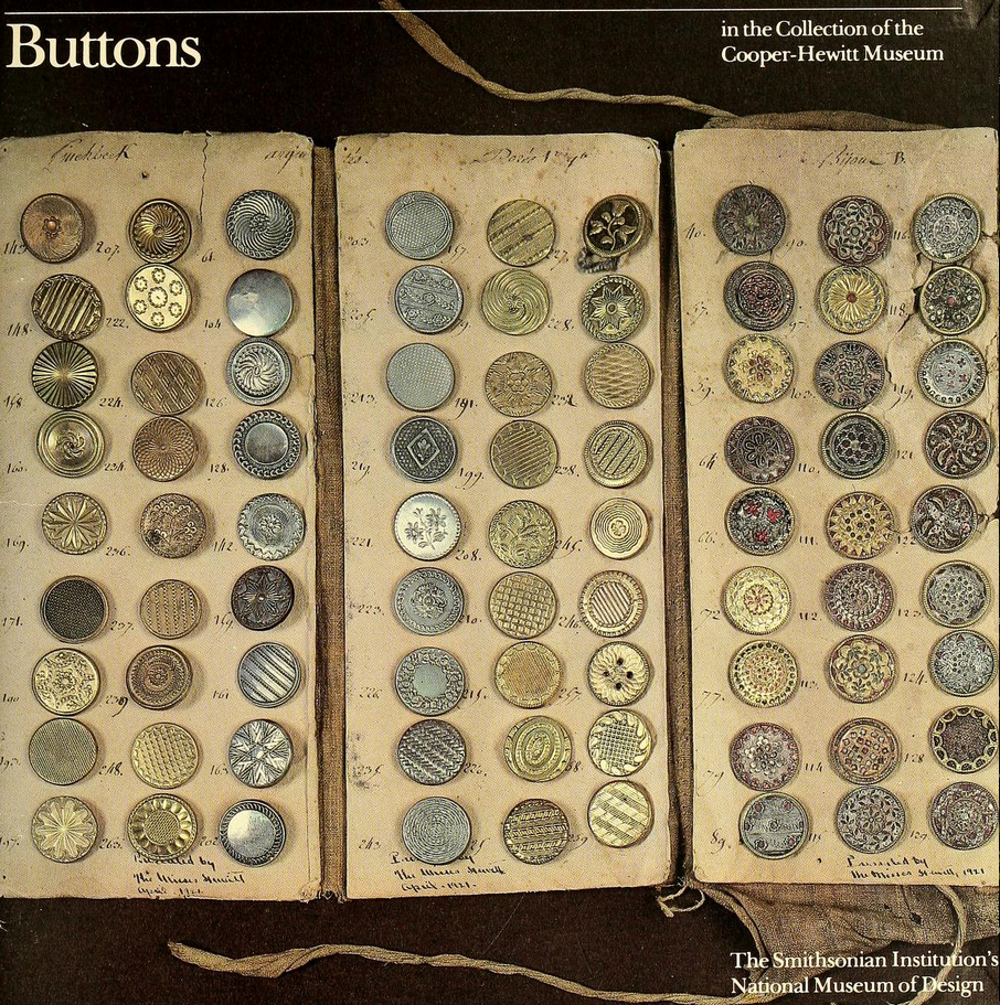 a grid of many old-looking buttons of different materials laid out on cloth