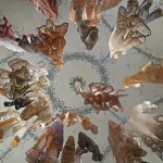 A photograph taken from the ground looking up at various brown, white, and orange garments hanging from an ornate ceiling.