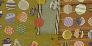 On the left is a mustard yellow textile with a variety of patterned circles of different colors sewn on top. One the right side, a brown, white, and yellow striped textile with more patterned circles sewn on top.