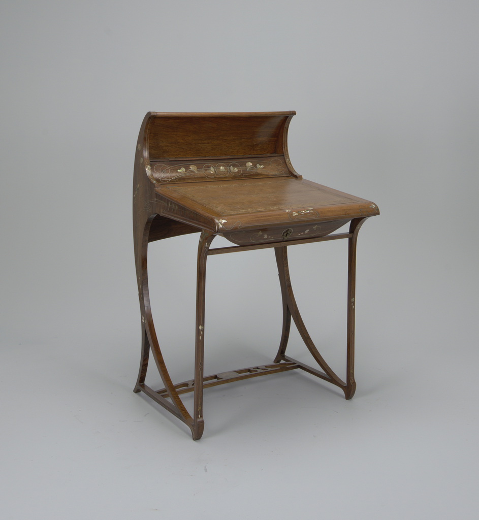 Small writing desk with curved back continuing in natural curve down the back legs. Liftable writing surface inset with stamped leather. Surface on all sides decorated with Oriental design of petals of mother-of-pearl and entwining lines of brass and silver alloy.