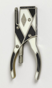 Narrow, rectilinear stapler with curved hand grips; sides decorated with overall geometric black and white enameled pattern.