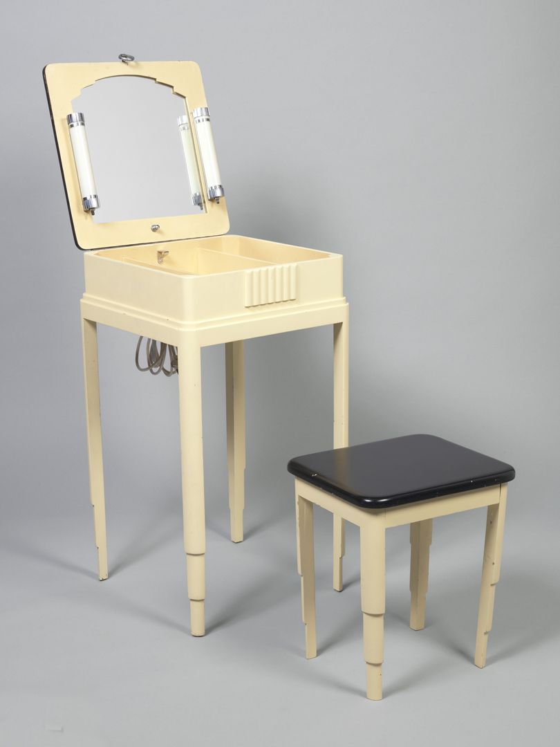 Ivory colored square-topped vanity table with black-lacquered lid, hinged at back, that opens to reveal mirror and two long lights; four tapered and stepped legs. Lacquered square-topped stool with tapered and stepped legs.