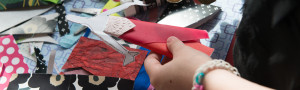 a childs hands holding a handmade paper doll, with paper and materials all around