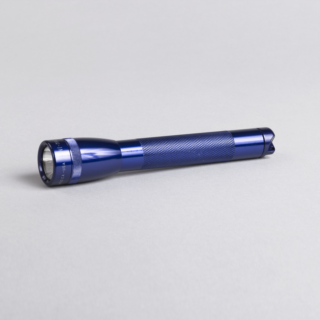 Blue-purple toned long cylindrical shaft, with knurled grip section, topped by narrow tulip-shaped head with clear lens. Removeable circular cap at end unscrews to reveal battery housing; spare bulb stored in cap.