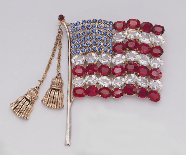 Right-facing American flag consisting of 48 blue paste “stars,” in upper left; alternating red and white “stripes” (22 red glass paste “rubies” and 22 transparent glass paste “diamonds”) unfurled on a gilded metal flag pole with two free-swinging tassels suspended from fine link chains at the top; the tassels fringes hinged at the neck, allowing for movement.