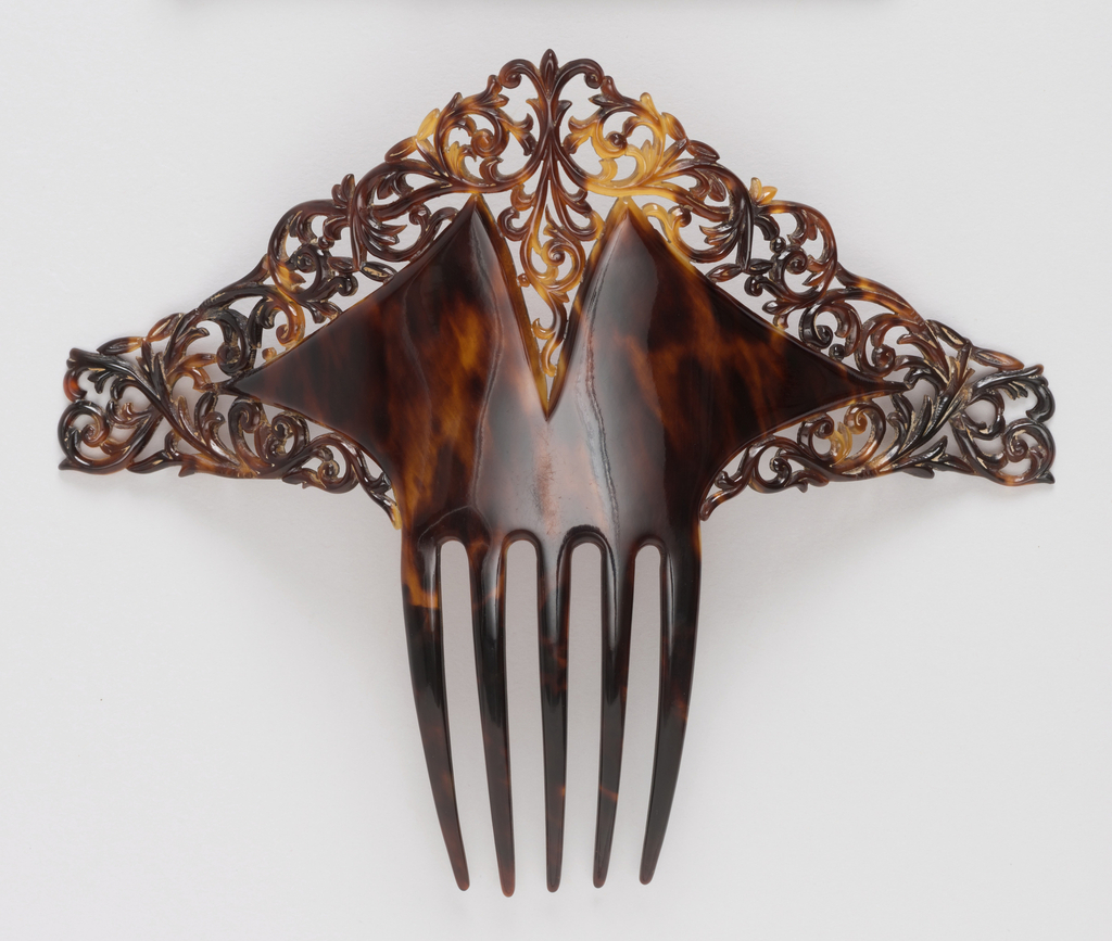 Image features a decorative comb of triangular form, made of mottled, translucent brown tortoiseshell. The edges with intricate pierced scrollwork surrounding a solid section with a V-shape cut in the center; five long teeth at bottom, to fix the comb in the wearer's hair. Please scroll down to read the blog post about this object.