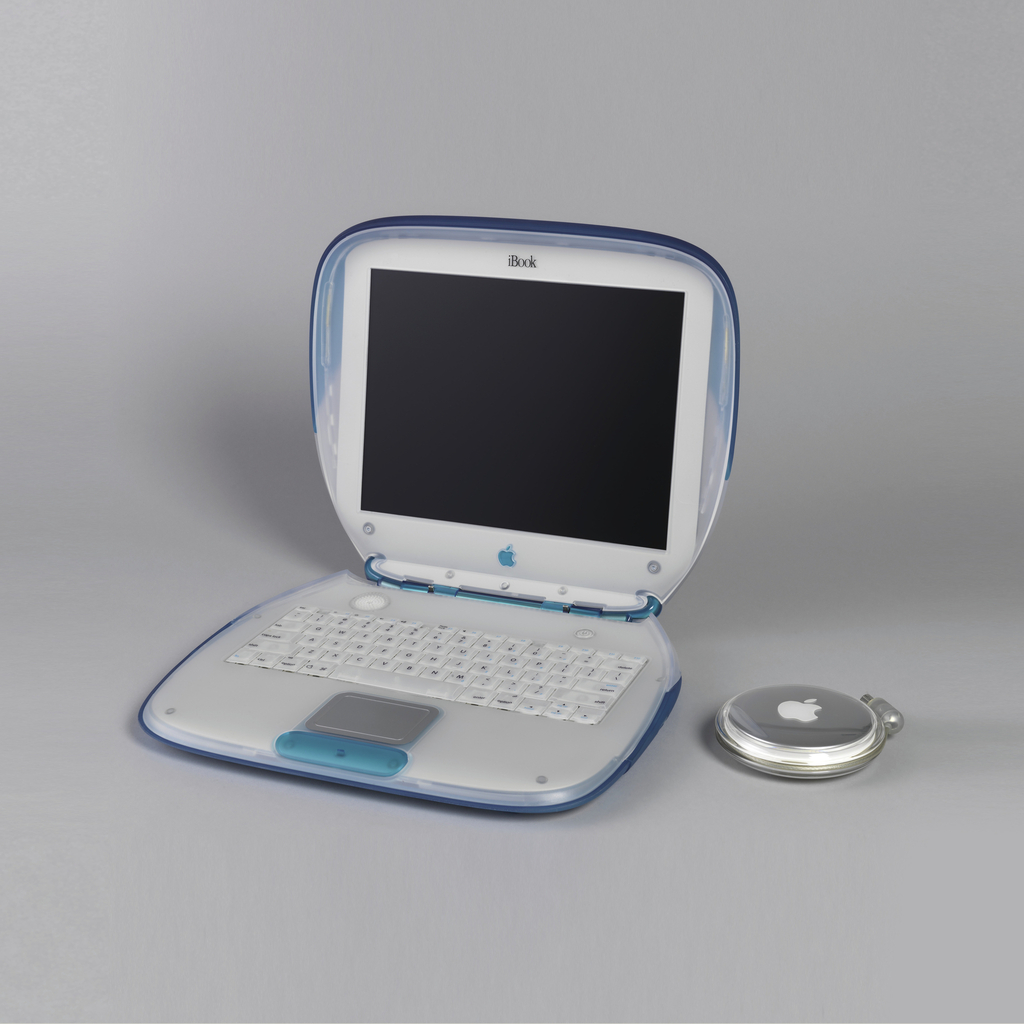 Image features a laptop computer with a rectangular body with rounded corners, the housing of translucent clear and blue plastic with blue pull-out handle at back. The hinged lid opens to reveal a screen and an inset keyboard with function keys, a touch pad, power button and a small speaker. Separate disk-shaped clear plastic and metal power adapter contains windup cord. Scroll down for the blog post related to this image.