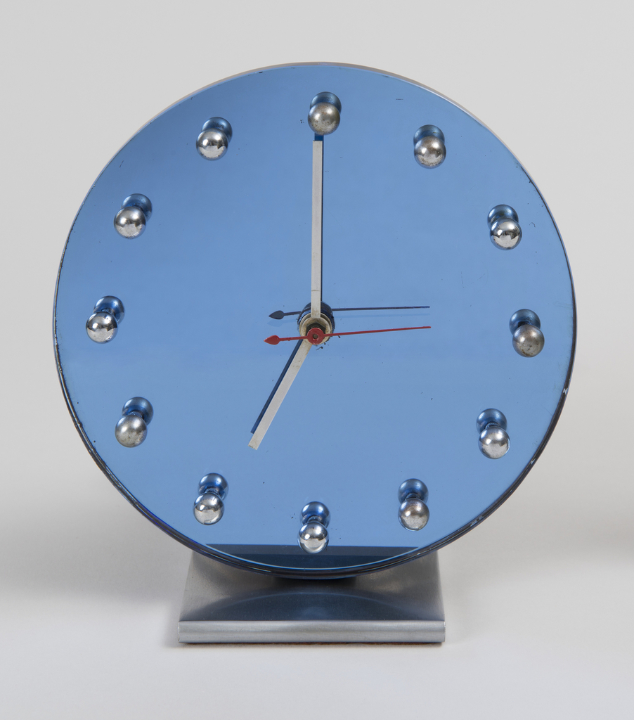 This is a clock. It was designed by Gilbert Rohde and manufactured by Herman Miller Clock Company. It is dated 1933. Its medium is glass, chrome-plated metal, enameled metal.