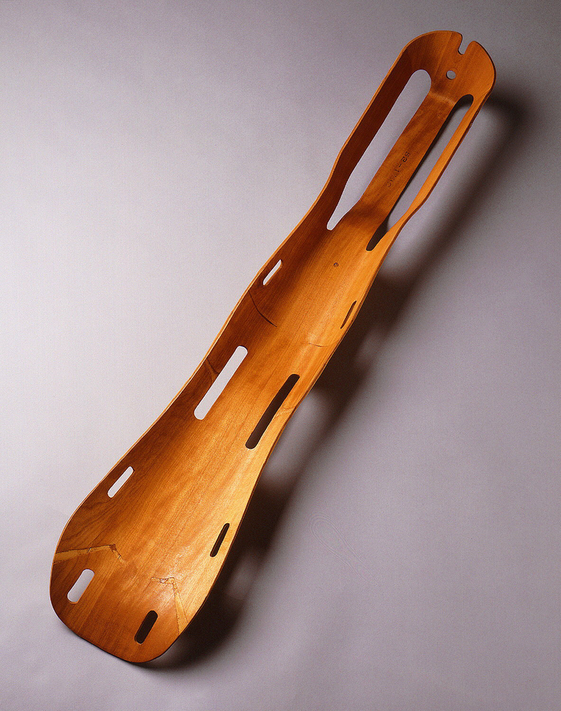 Image features a thin-walled molded plywood form contoured to follow the shape of the back of a leg. There are eight openings over the length of the splint to accommodate straps for securing an injured leg.