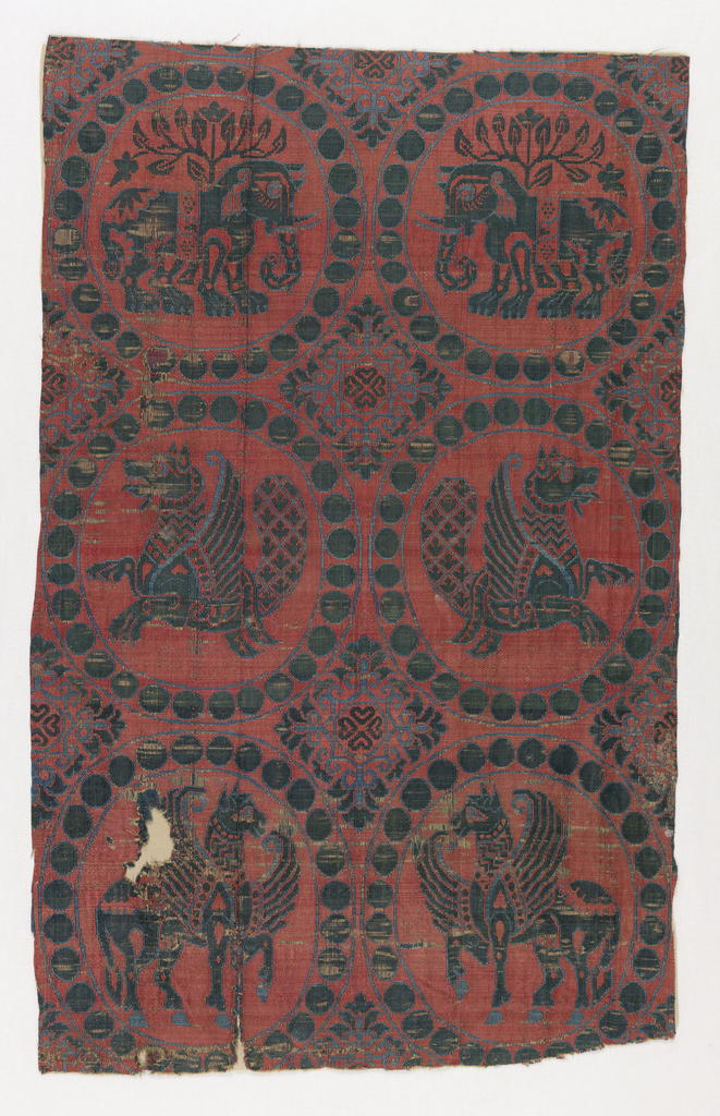 Fragment of woven silk containing six pearl roundels, in sky blue and dark green on a red ground. The top two roundels enclose confronted elephants, the middle two addorsed senmurvs, and the bottom two confronted hippocampi. Four-lobed rosettes with elaborate floriated edges in interspaces.