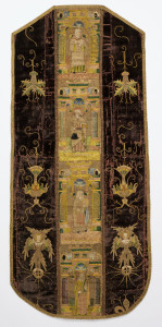 Back of a chasuble with an embroidered orphrey band down the center, embroidered motifs at the sides, and bound all around with gold braid. The deep brown velvet side panels are embroidered in gold metallic and polychrome silks with angels on orbs and floral arrangements. The center band is densely embroidered with four saints in different architectural niches.