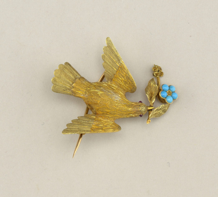 a gold brooch shaped as a bird with a twig in its beak sprouting leaves and a flower made of turquoise