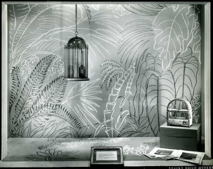 two birdcages on display in a storefront window against a background pattern of palm fronds