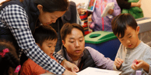 A man and a woman help two young children with an activity at a table.