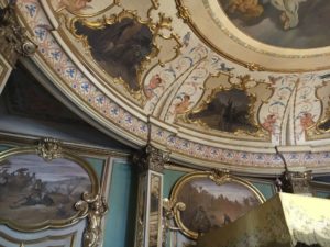 Detail of rococo paneling inside an architectural interior. Four paintings surrounded by ornate frames are visible.