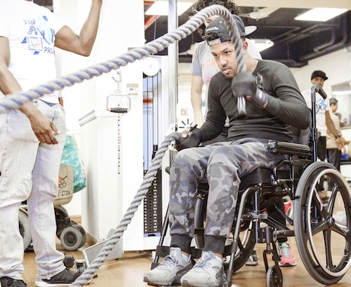 An image of a man in a wheelchair taking part in a strengthening exercise with ropes at The Axis Project.