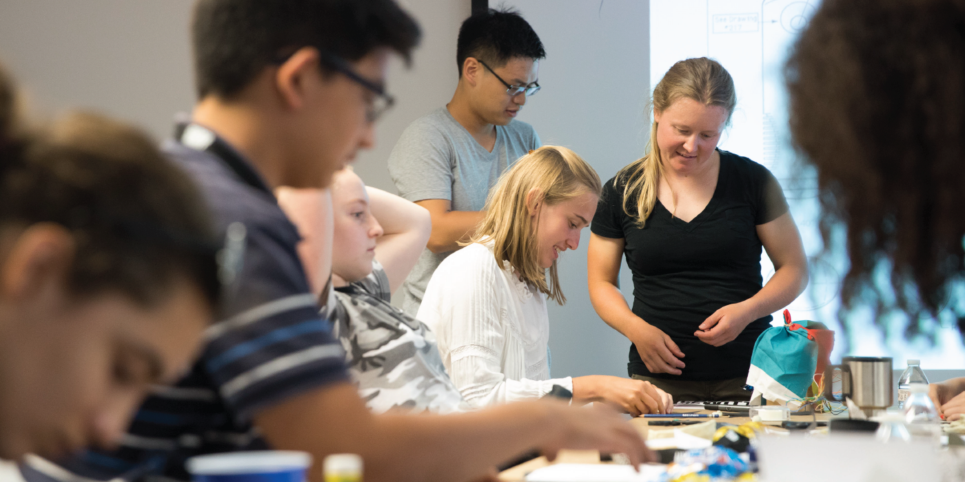 Photograph of seven teens around a table working on a prototype.