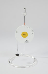 Circuar hanging scale with white outer circle with increments in ponds around outer edge. Yellow center with Braun logo. Wire hook at top and wire arm with foam semi-circle end at bottom. Please scroll down for a blog post about this object.