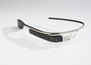 Image features eyeglass-like wearable technology with titanium frame that is a plain band on the left side and on the right side holds a clip-on camera, computer, battery, and speaker. Please scroll down to read the blog post about this object.