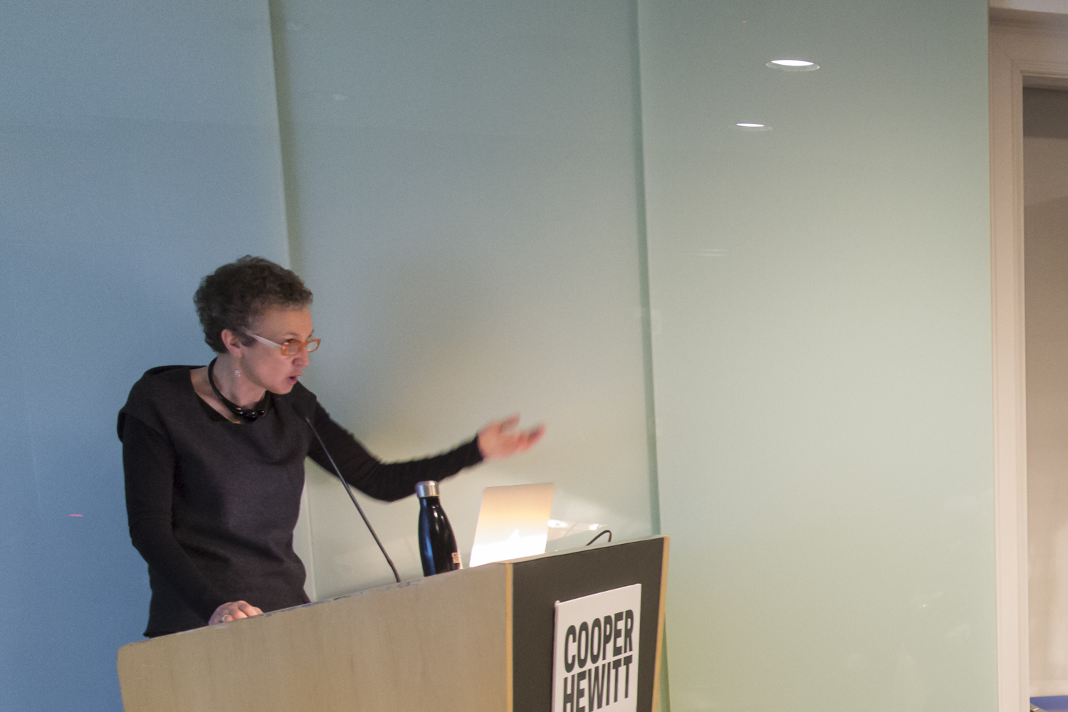 During the Morse Historic Design Lecture, Beatrice Quette, a woman with short curly dark hair lectures from the podium at Cooper Hewitt while audience members look on.