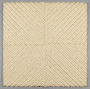 The natural linen woven base cloth is stretched in tension on a wooden frame. Skeins or coils of bleached linen are alternately twisted in the 's' or 'z' directions, and anchored to the foundation by sewing them with strong linen thread using a semi-circular needle, allowing the artist to control and stabilize the volume.