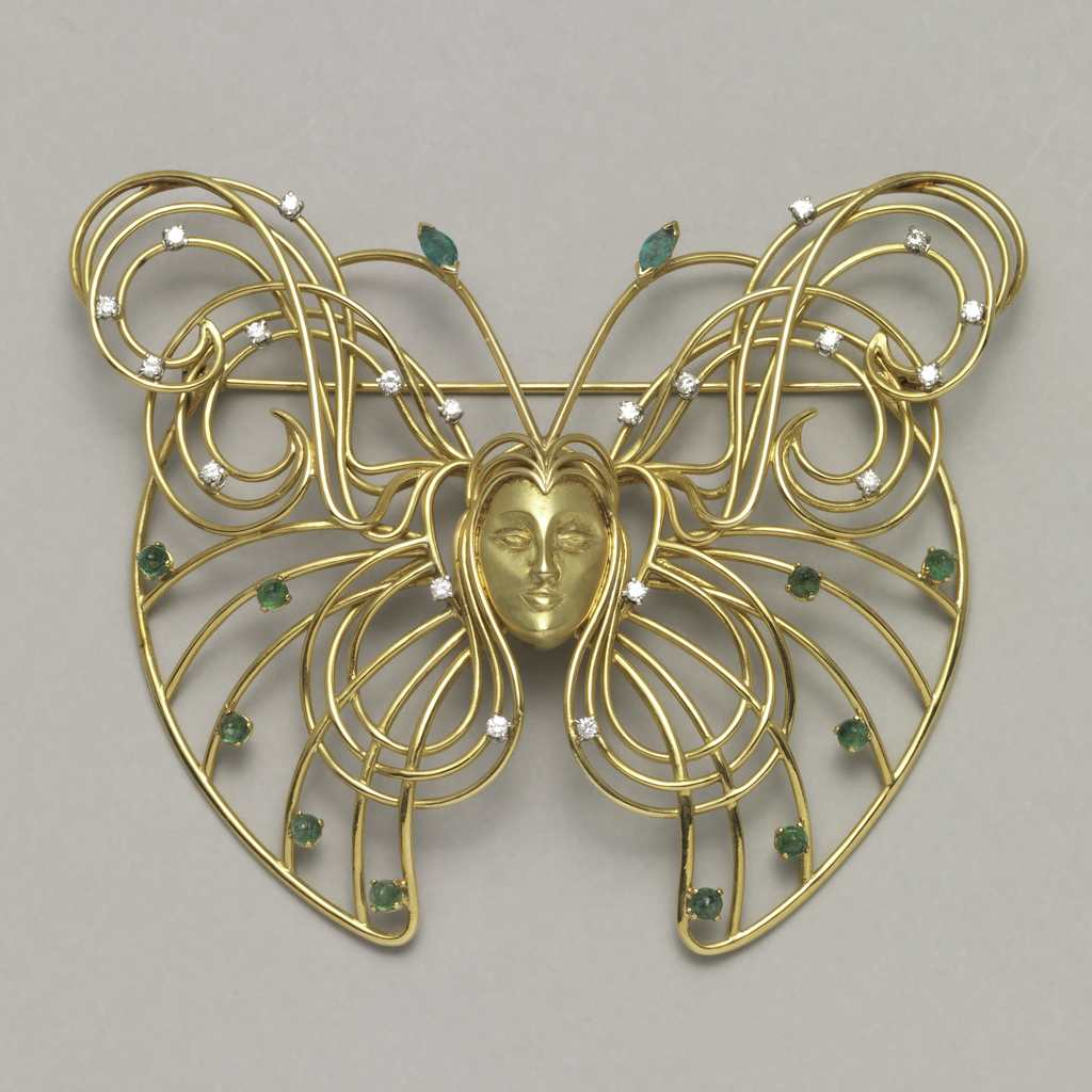 Image features brooch in butterfly shape made of thin gold wire, with face of woman and hair coiled into butterfly’s wings; small diamonds and emeralds throughout. Please scroll down to read the blog post about this object.