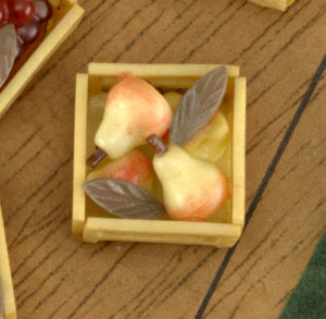Image features button in the form of an open-topped wooden crate containing four pears in tones of yellow to pink, with two narrow green leaves interspersed among them. Pease scroll down to read the blog post about this object.