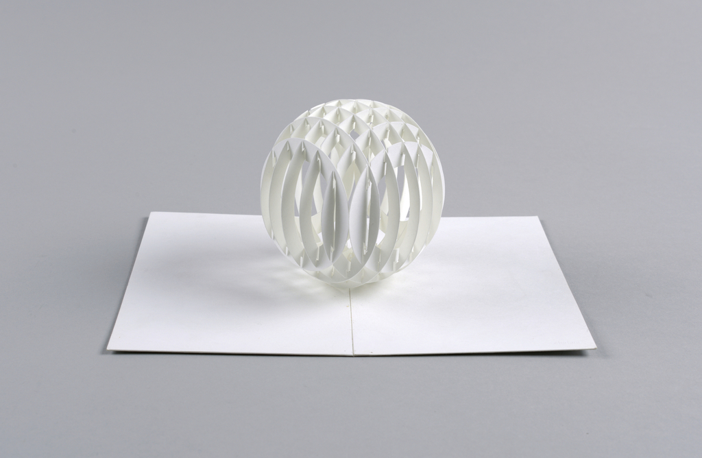 Image features a cut and folded white paper sphere that sits upright upon the center fold of a piece of paper. Please scroll down to read the blog post about this object.