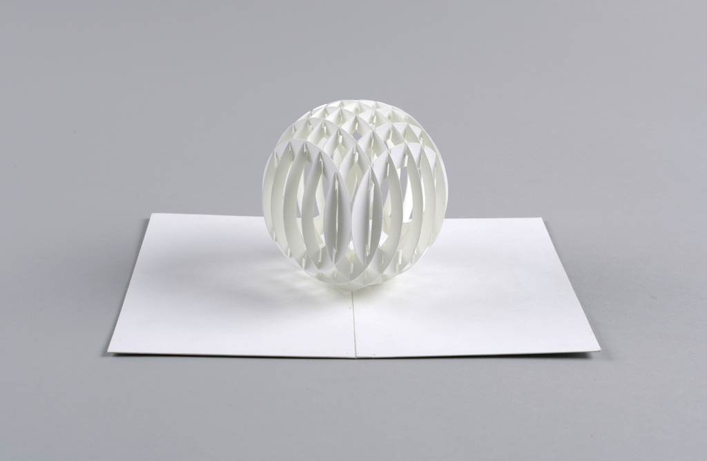 Image features a cut and folded white paper sphere that sits upright upon the center fold of a piece of paper. Please scroll down to read the blog post about this object.