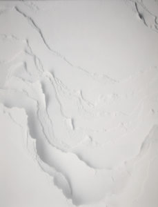 The image is a detail shot of a monochrome white wallpaper composed of torn and layered strips of paper. Please scroll down for a further description of this piece.