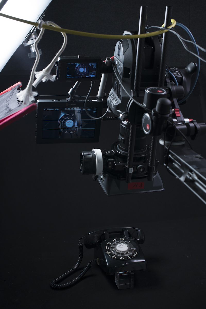 Black rotary telephone is on floor and camera is set up above it ready to capture a shot.