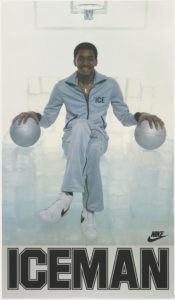Image features photograph of George “The Iceman” Gervin in a space filled with large ice cubes, holding a silver basketball in each hand, wearing a silver tracksuit with the word: ‘ICE’ embroidered on the chest. He wears white Nike sneakers. In lower margin: ICEMAN; lower left of photograph: NIKE logo. Please scroll down to read the blog post about this object.
