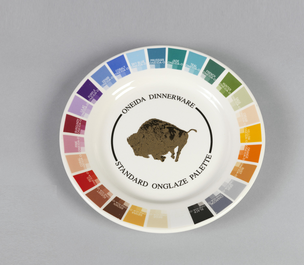 This image features a circular sample plate glazed with squares of various colors around the rim, surrounding the logo of a running buffalo in gold, all on a white background. Please scroll down to read the blog post about this object.