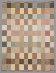 Small-scale rectangular weaving with a checkerboard pattern of squares in soft shades of brown, tan, green, and pink.