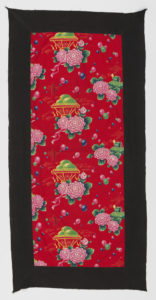 Image features: Quilt cover for a single bed. Bright red ground is printed with dahlias that resemble the paper flowers that were awarded to workers. In the center is a yellow basket with tassels swinging and with three yellow-green mangoes. Behind the basket is the imperial ornamental pillar (huabiao) which is a symbol of political authority that stands in front of Tiananmen Gate. To the left is a drum, cymbals and a musical instrument called an erhu. Behind that motif is a building in which the mango possibly was exhibited. On the right is a bedroll and satchel with the Highest Directive sticking out. Colored balloons float above. Please scroll down to read the blog post about this object.