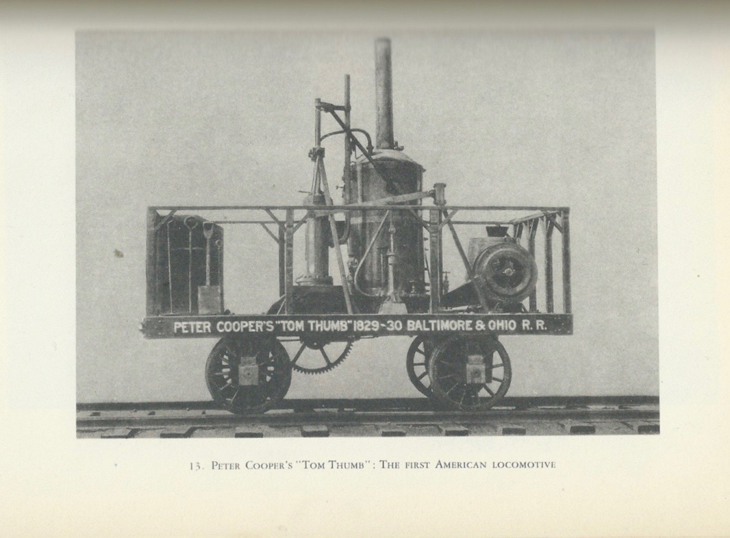 This image is a scan from a book. The page features an image of a locomotive vehicle on tracks. Four prominent wheels support a fenced-in platform that houses shovels and various pieces of machinery. Wording on the platform reads 