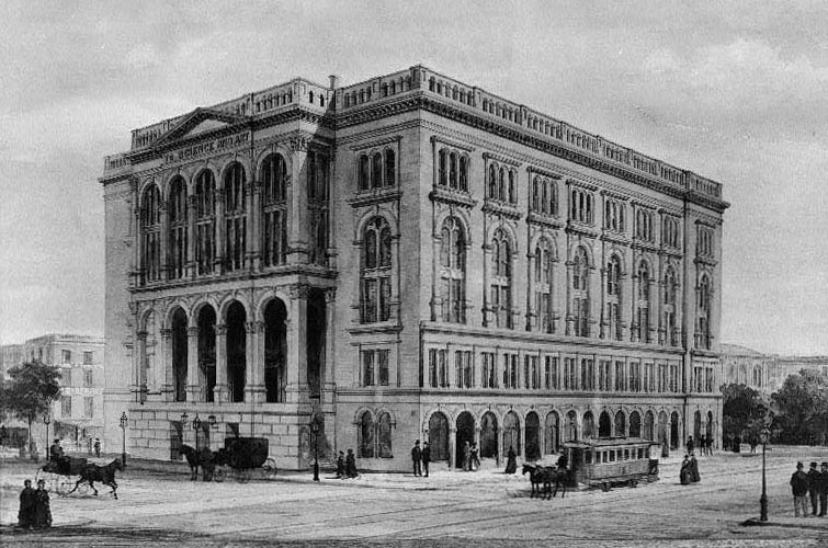 This image shows a large, four-story building, pictured here from a nearby intersection. Small groups of people and horse-drawn carriages populate the streets in front of it. Trees and light posts also line the streets. The building is box-like and exhibits Palladian architecture, with a restrained facade composed of windows framed by columns and arches.