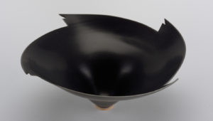 Four Clipped Wings Bowl, 1984. Thrown porcelain bowl. From narrow circular foot, body flares upward and outward at extreme angle. Upper edge cut with four wing-like notches. Overall surface smooth,,with modulations. Exterior and interior with semi-matte black glaze; foot ring glaze orange-brown outside. Created by Elsa Rady