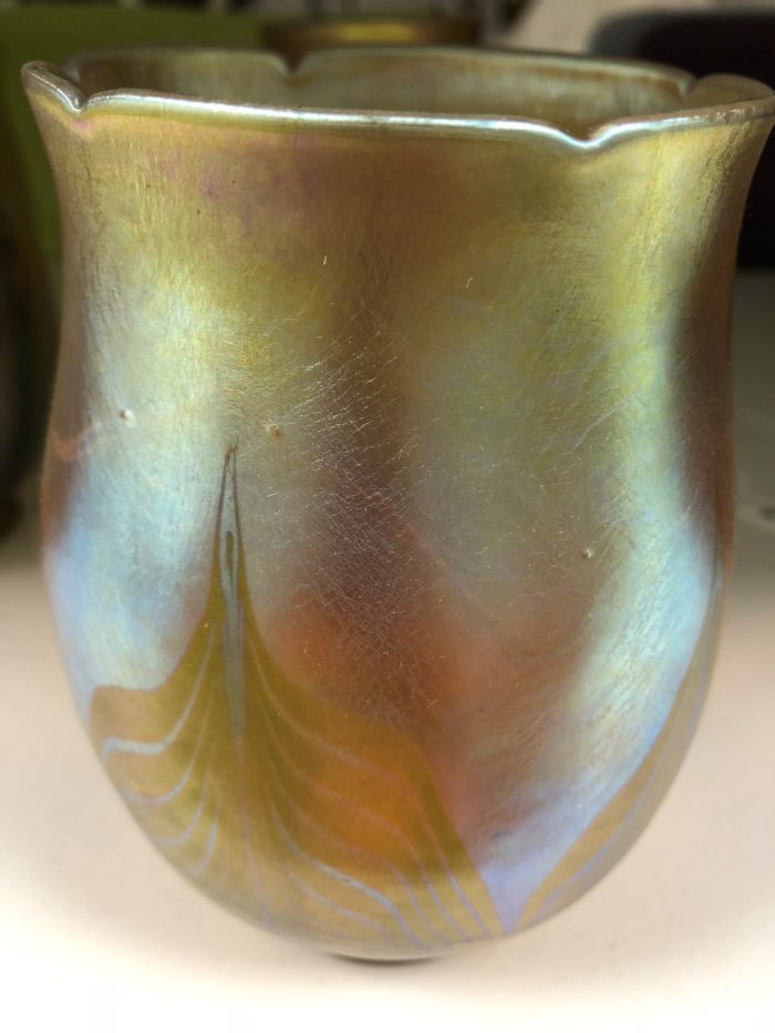Vertical image of a small iridescent vessel. The vessel is shaped like a tulip flower. Its colors are shimmery yellows, oranges, and greens.
