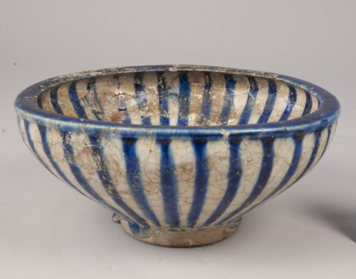 Image of a flaring bowl with incurvative rim. Greenish-white glaze, running in heavy drops on outside. Painted with radiating blue bands on inside and outside, and blue band on rim. Some of the component parts iridescent.