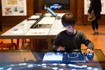 A young boy uses his finger to sketch a design on an interactive table in the museum.