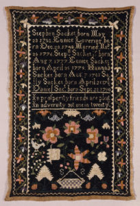 Image features a rectangular sampler, in the upper half, a record of the births of members of the Sacket family: Stephen Sacket born May 23 1752. Eunice Lovering born Dec. 23 1748. Married Nov. 25 1776. Steph'n Sacket Jr. born Aug 7 1777. Eunice Sacket born April 25 1779. Hannah Sacket born Aug 7 1781. Sally Sacket born April 21 1786. Daniel Sact. born Sept 23 1790. Followed by a verse: "In prosperity friends are plenty In adversity not one in twenty." With scattered floral motifs and the initials SS in the lower half, and a floral border on three sides. The black background is embroidered on natural colored cloth. Please scroll down to read the blog post about this object.