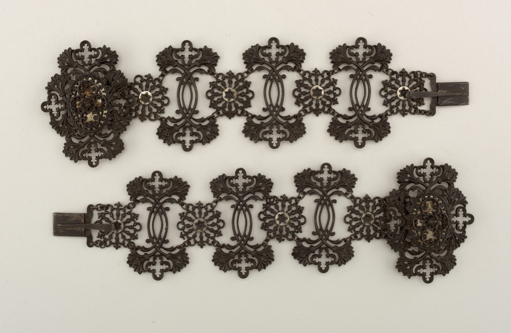 Image features pair of bracelets, each a wide, flexible, linked band comprising three black-toned openwork segments with a quatrefoil-and-foliate pattern alternating with rosettes, all in Gothic Revival style. Please scroll down to read the blog post about these objects.